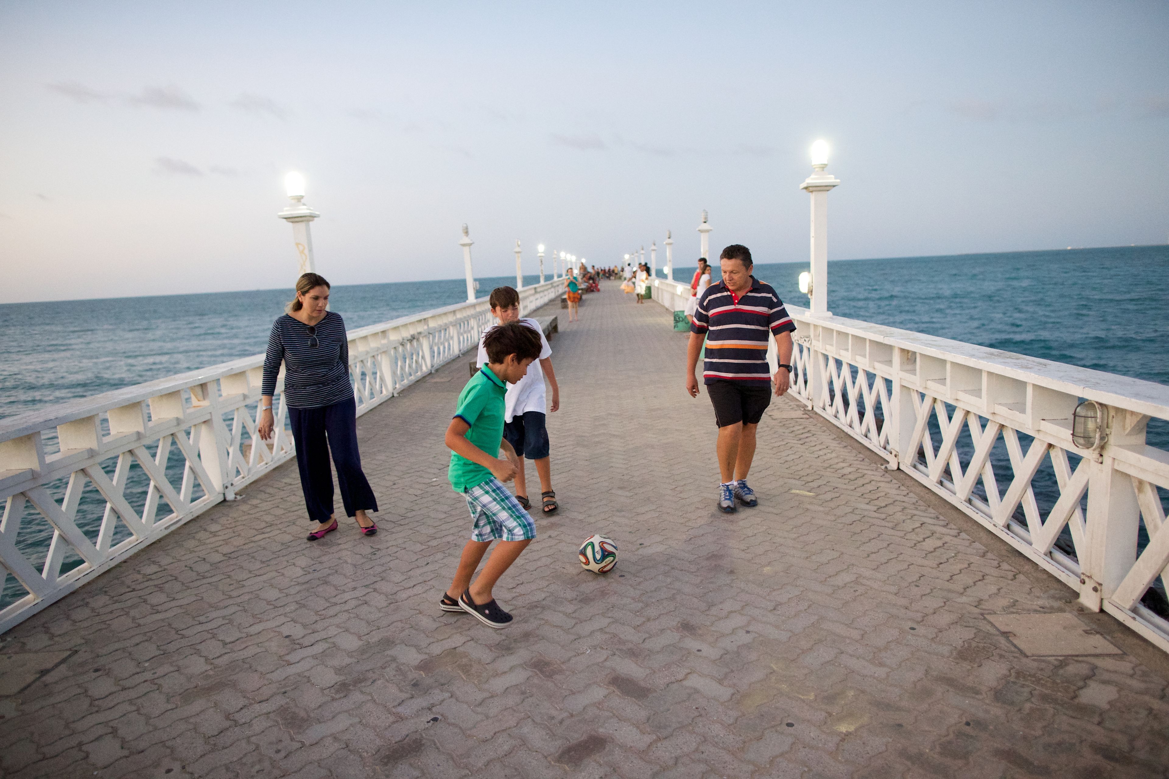A family kicks a soccer ball on a pier.