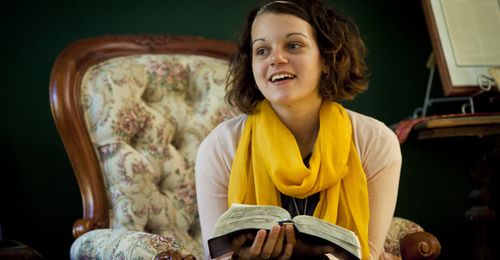 A Young woman holding open scriptures. She is looking up and smiling.