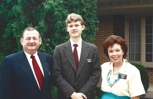 young missionary elder standing in between older couple