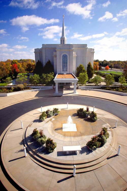 The fountain on the grounds of the St. Louis Missouri Temple, with the temple in the background and a view of the grounds surrounding the temple.