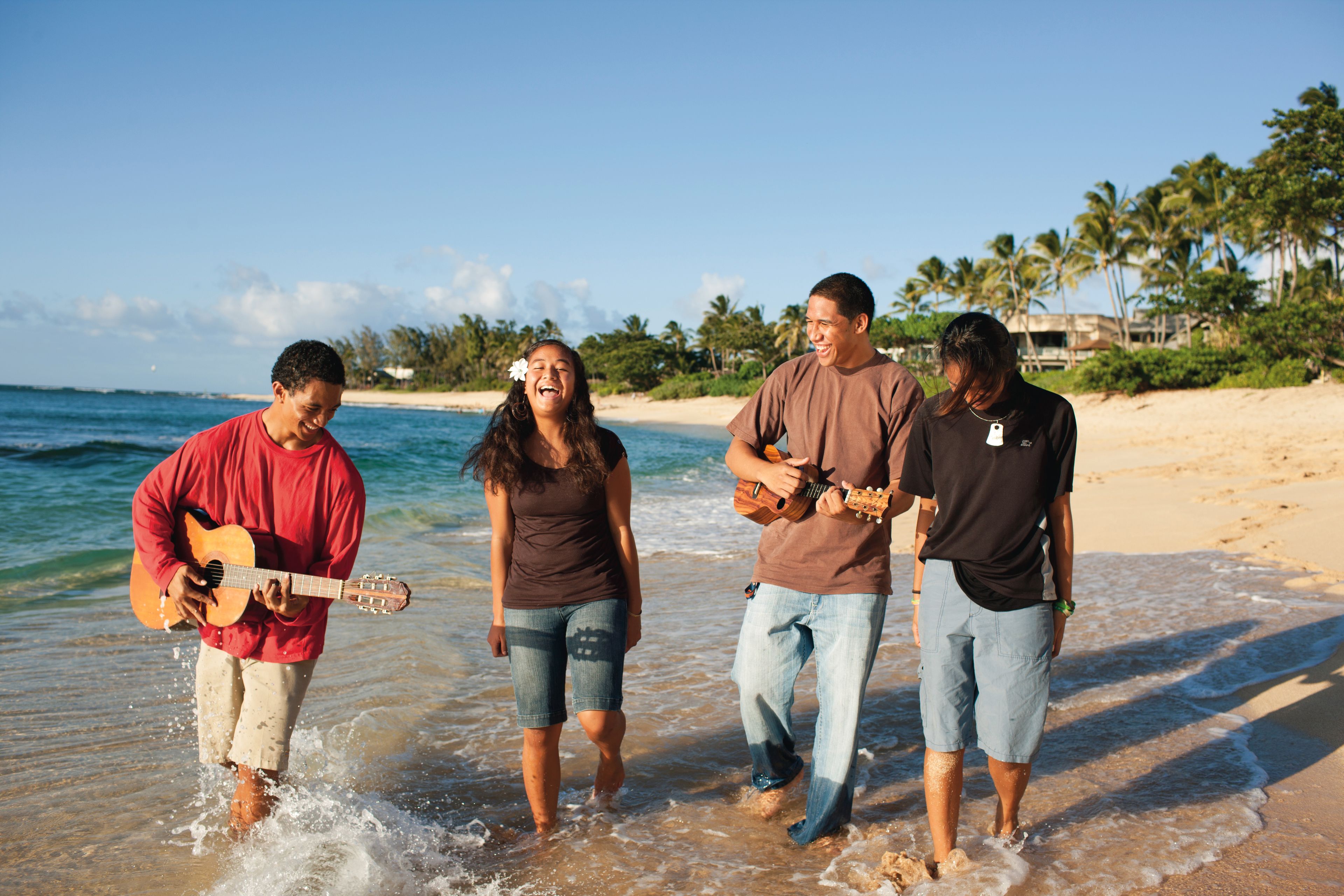 Some young men and young women play music and walk along the beach together.