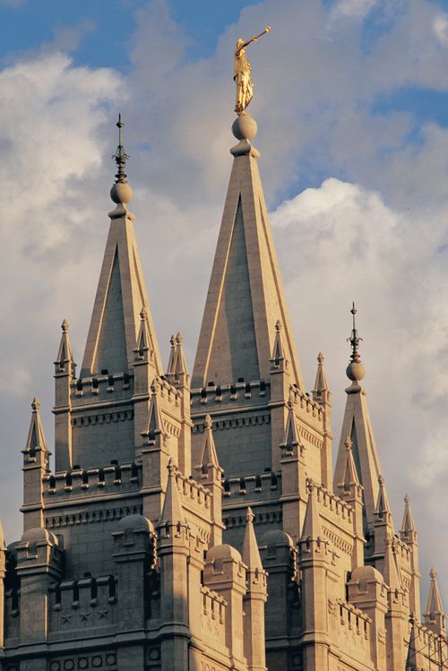 The east spires of the Salt Lake Temple with the Angel Moroni and clouds in the sky.