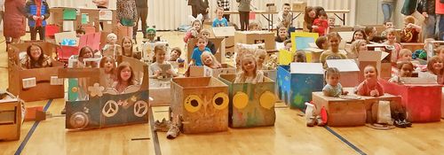 Children sitting in cardboard boxes that have been decorated to look like cars
