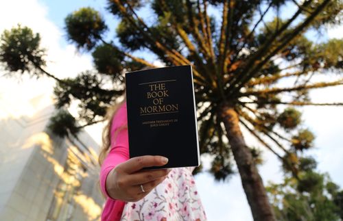 a woman standing in front of a temple and holding a Book of Mormon