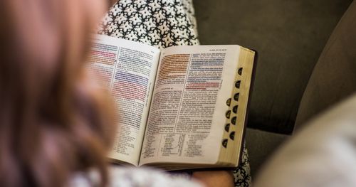 Young woman sitting in home reading open scriptures that have been underlined. (horiz)