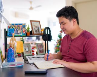 A young man sits in his home in Malaysia. He is studying.