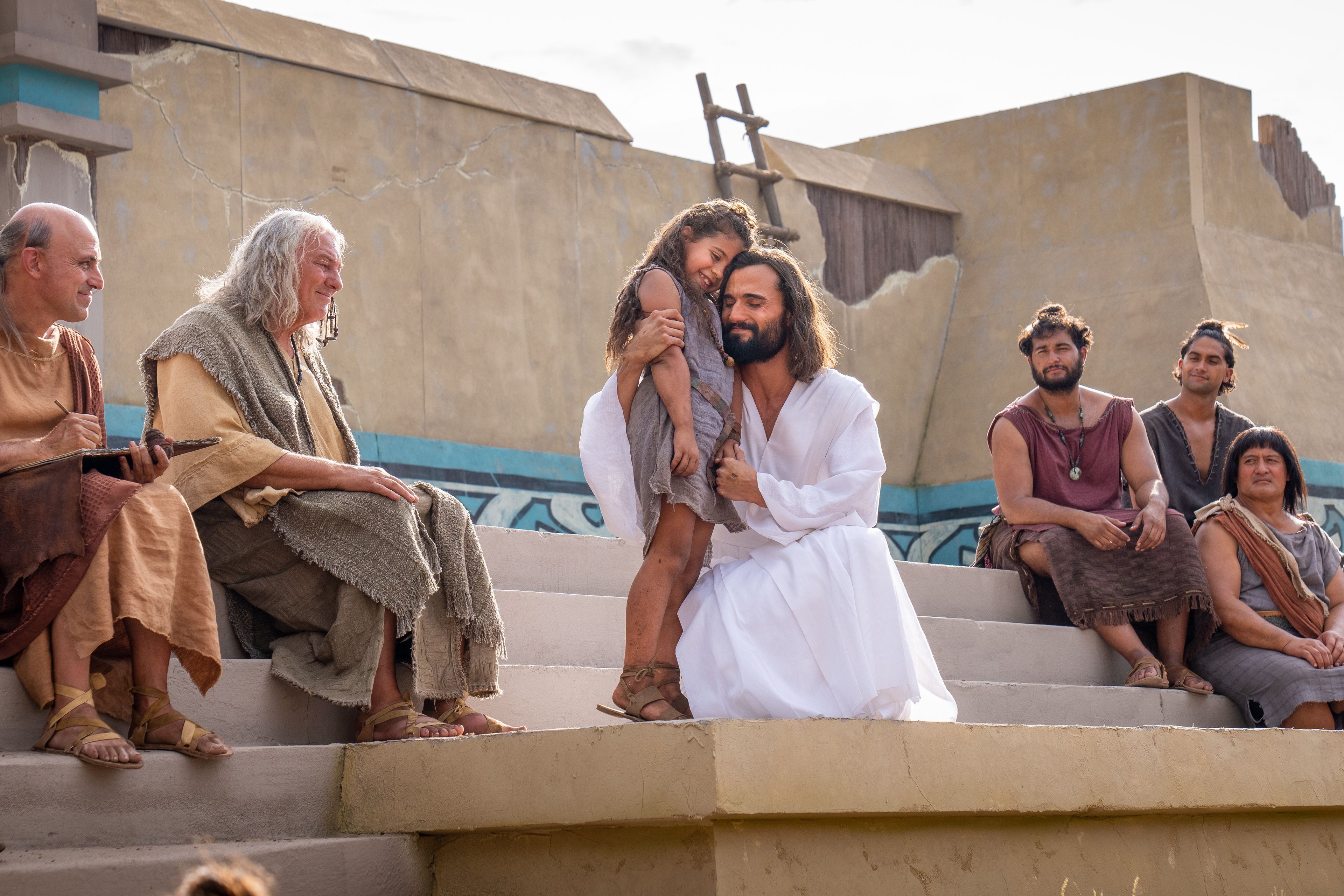 Jesus Christ greets Nephites on the steps of the Bountiful Temple. He embraces a young Nephite girl.