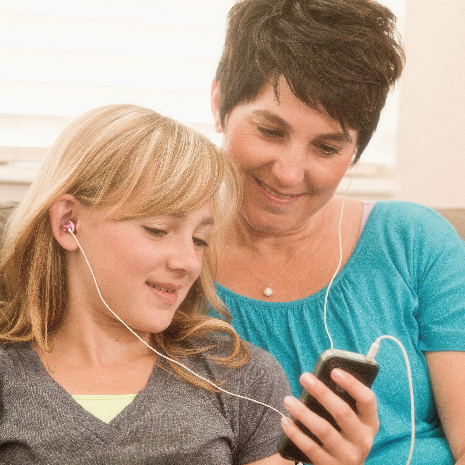A mother and daughter listen to music on headphones together.