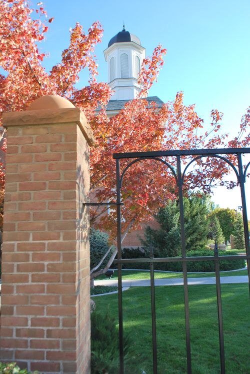 The gate to the grounds of the Vernal Utah Temple, with a view of a spire rising above the top of a tree.