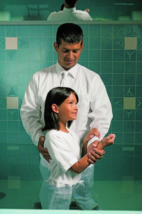 A man baptizing a young girl.  They are standing in the font.