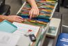 Woman's hands searching for file in filing cabinet. Tops of colored files show. (horiz)