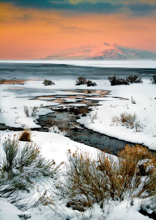 A stream runs through Antelope Island, with snow on the ground and a mountain in the background.