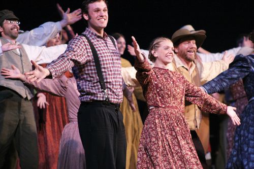 A group of actors and actresses from the Nauvoo Pageant standing with open arms and smiling.