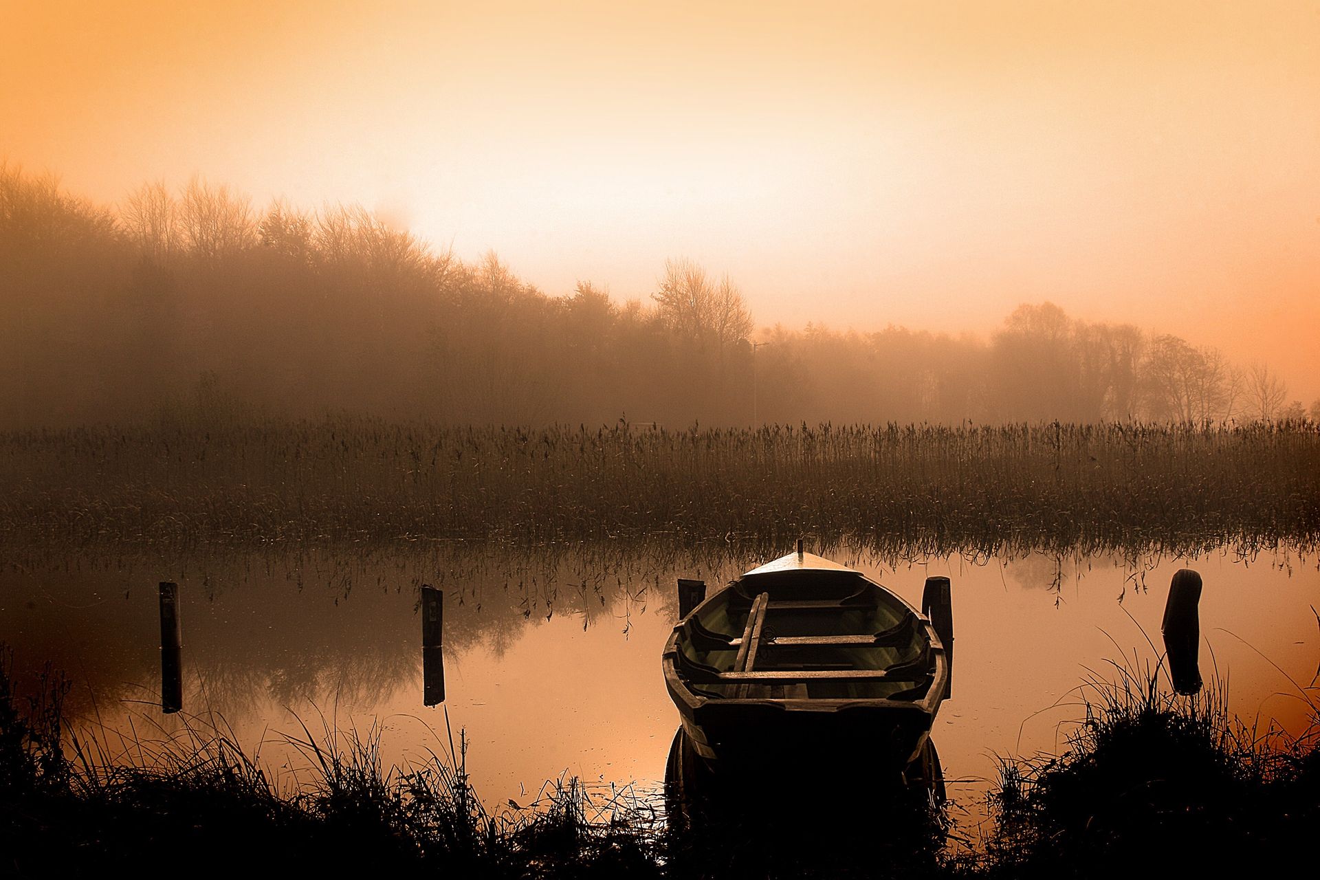 The sun rises over a lake with a rowboat.