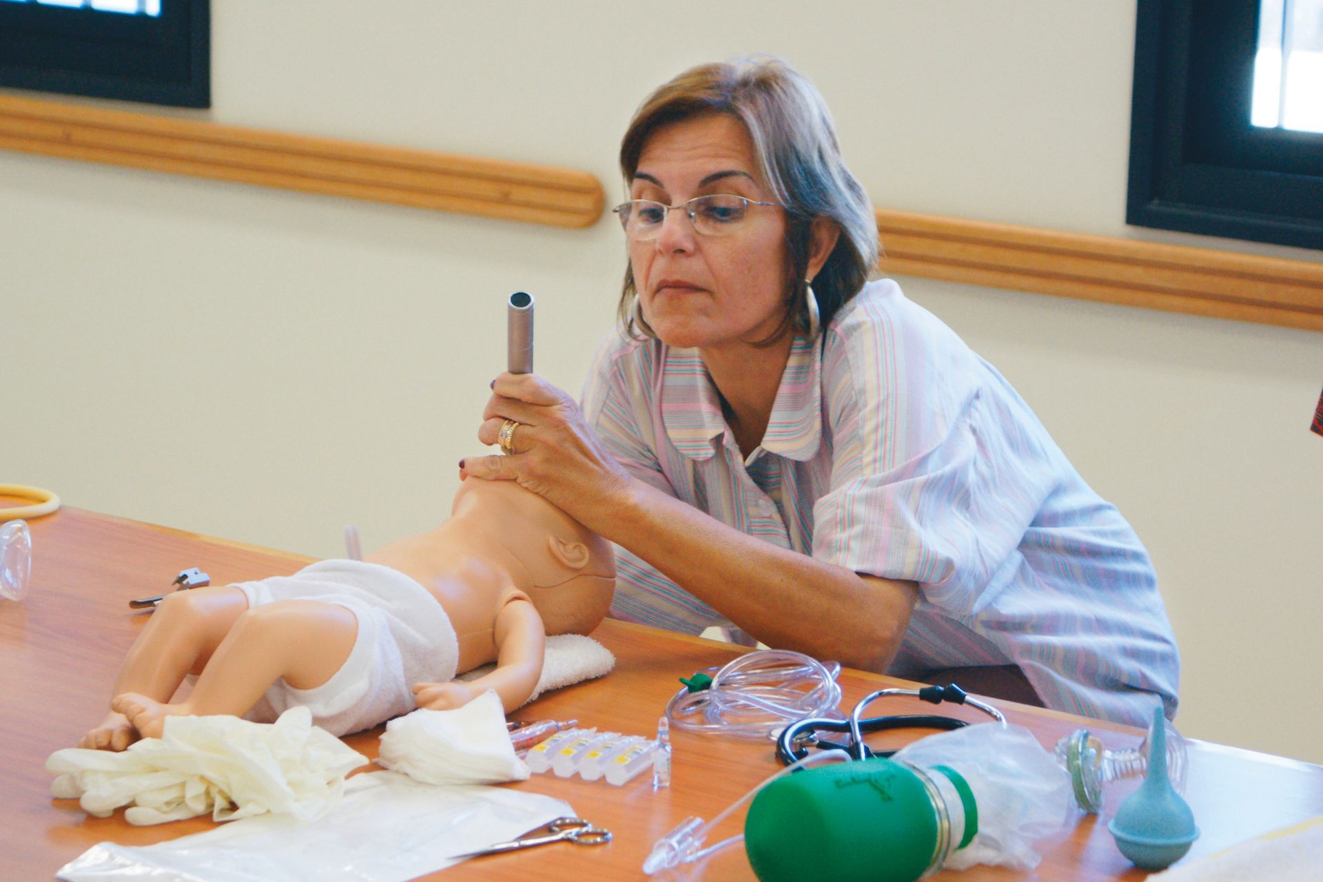A woman at a table looking inside the mouth of a CPR practice baby at a welfare program workshop in Brazil.