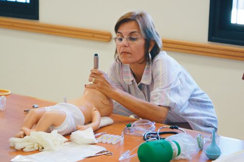 A woman sitting at a table and looking inside the mouth of a CPR practice baby at a welfare program workshop in Brazil.