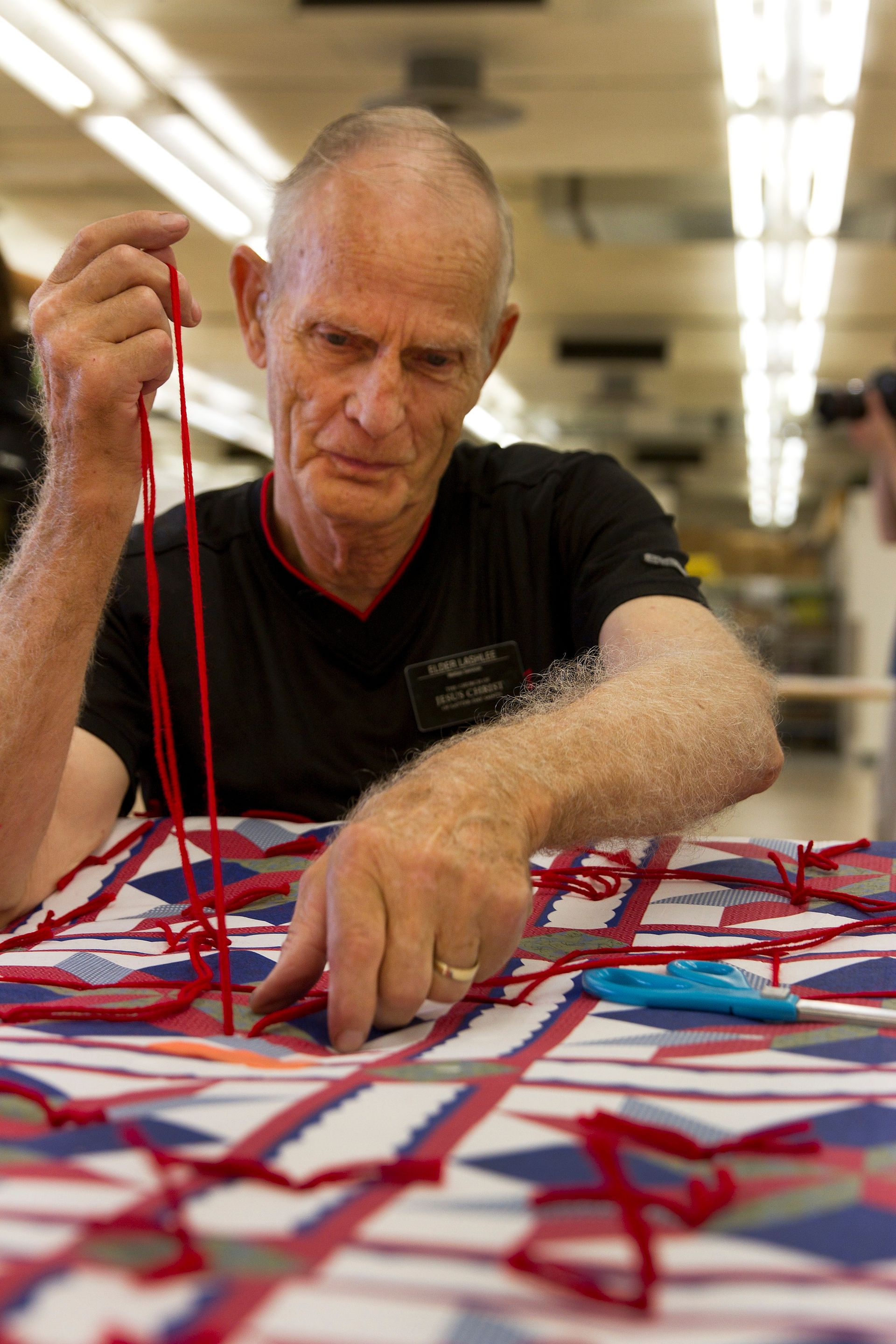 A senior missionary helps tie a quilt at a humanitarian center.