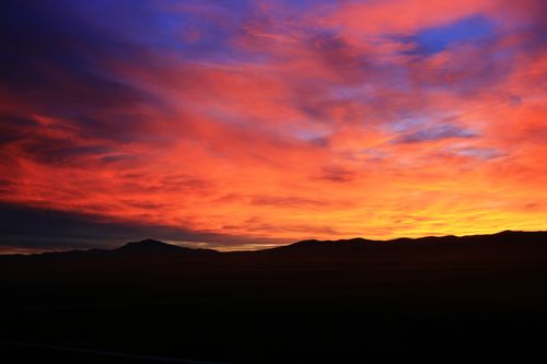 A low landscape is silhouetted by the sunset, which is red, blue, and yellow.