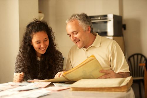 A father and daughter sit down at a table and look at family history documents together.
