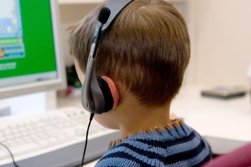 A boy in a blue striped shirt wears headphones and plays a game on the computer.
