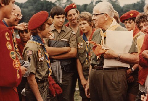 President Ezra Taft Benson in Scout uniform, holding a folder and standing with Boy Scouts, around 1977.