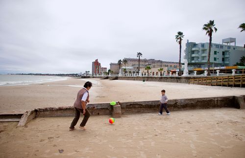 woman kicking a ball with a boy on the beach.