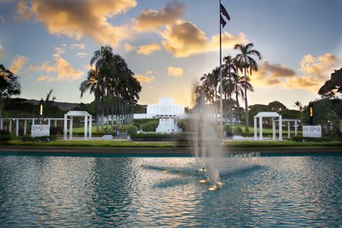 A large water feature on the grounds of the Laie Hawaii Temple, with the temple seen in the background in the evening.