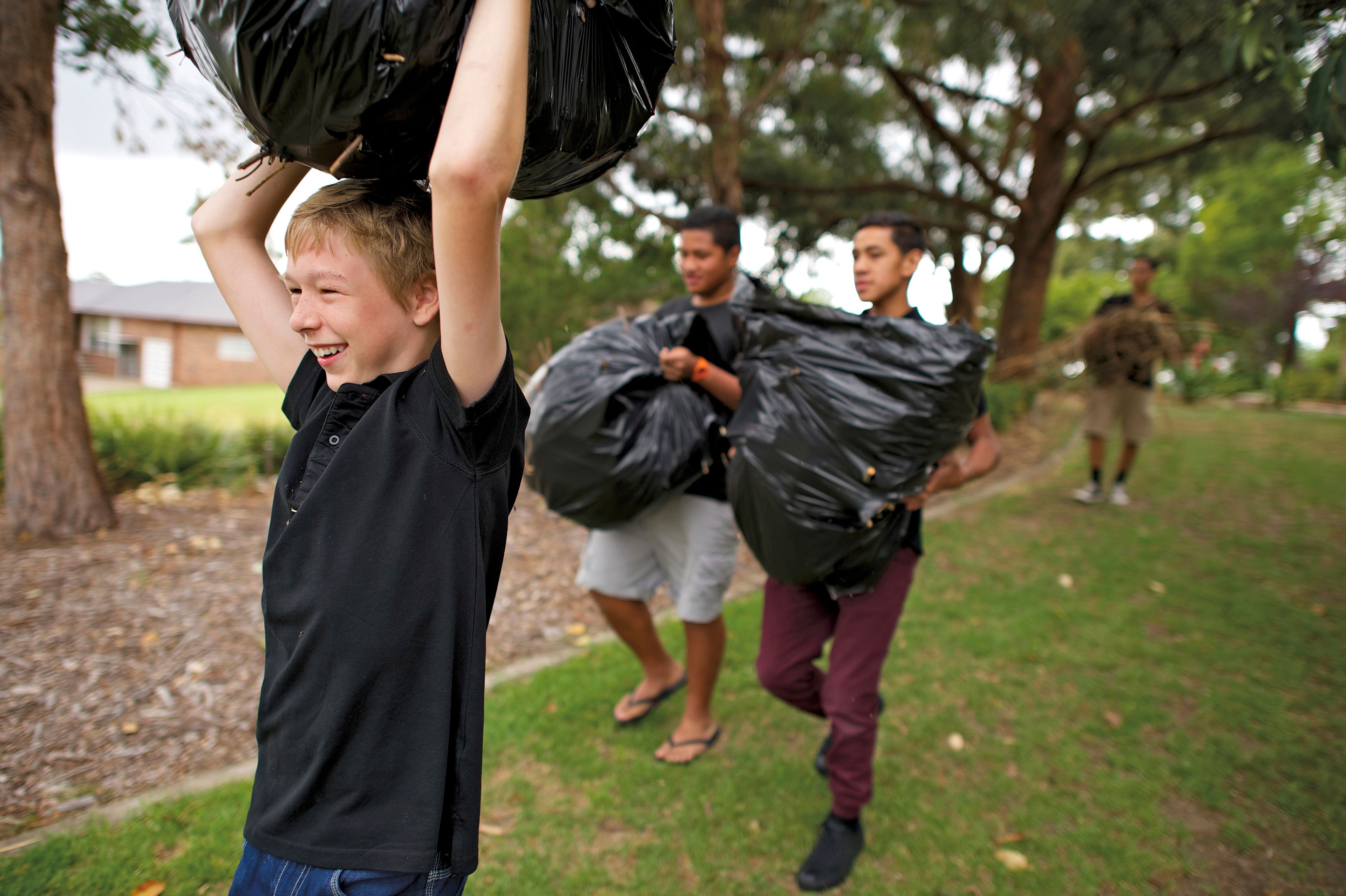 Three young men doing service, carrying black garbage bags full of leaves outside.  