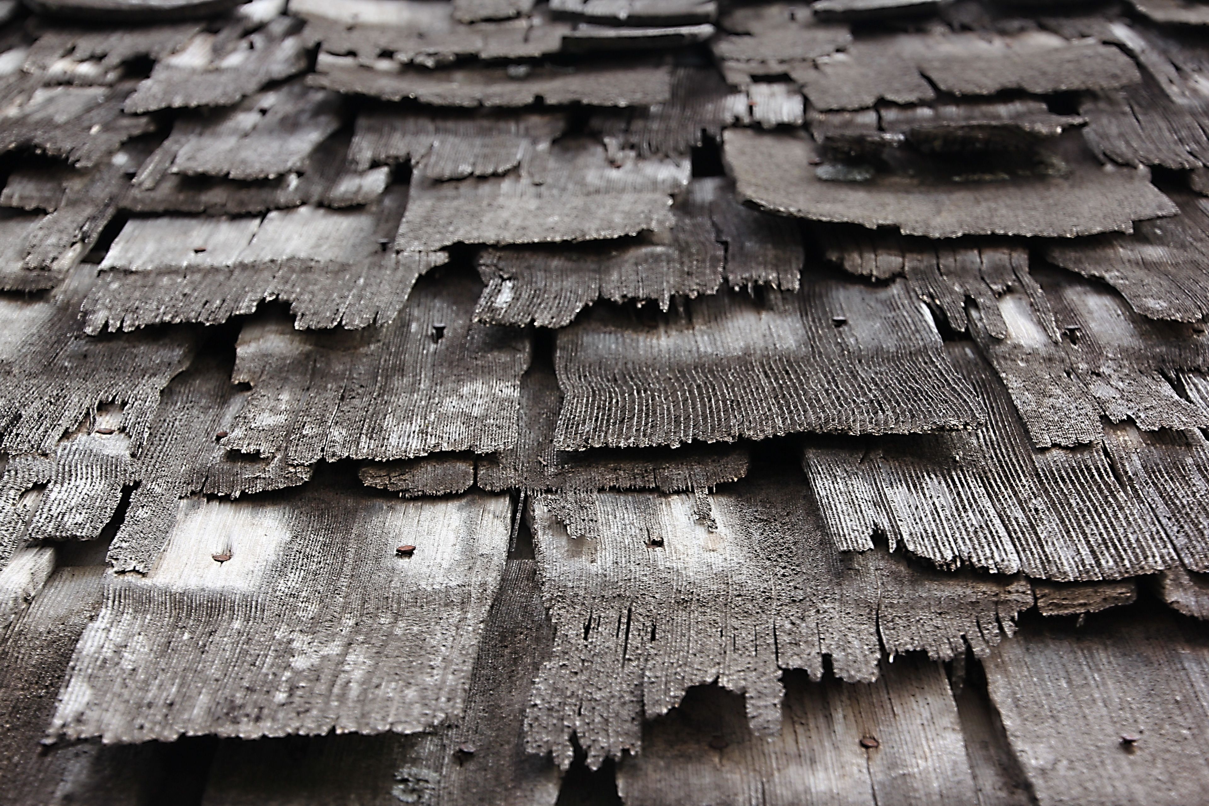 Old wooden shingles stacked in layers on a slanted surface.