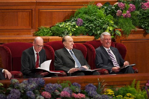 Thomas S. Monson, Dieter F. Uchtdorf, and Henry B. Eyring in red armchairs, smiling and holding black binders during general conference.