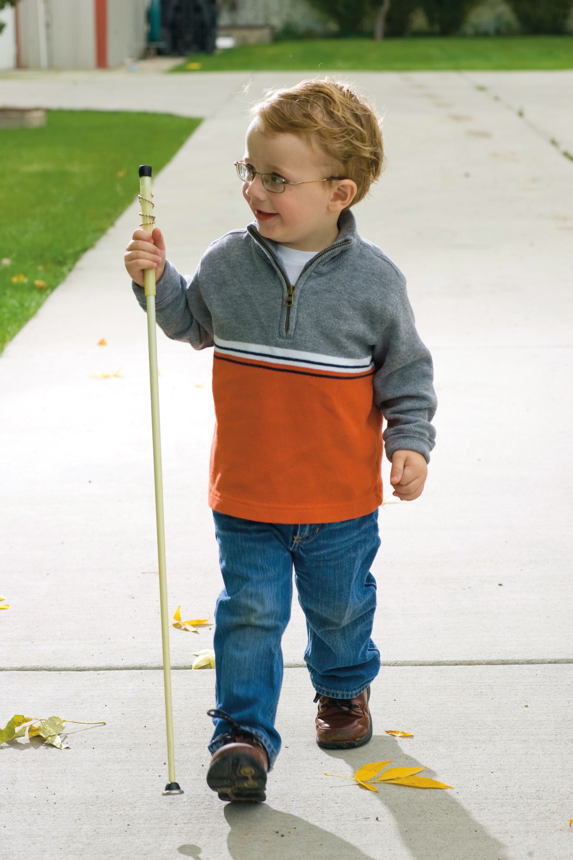A young boy using a white cane for the blind as he walks down a sidewalk.
