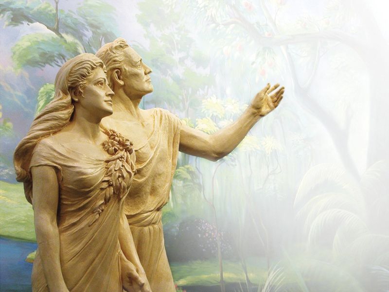 A statue of Adam and Eve in front of a mural.