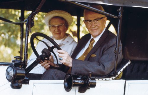 "President Ezra Taft Benson and Sister Flora Smith Amussen Benson riding in a car that says ""Just Married 50 Years"" on the door."