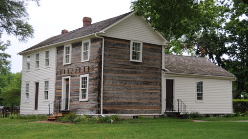 The expanded Smith Family Homestead building which is half log home and half white-painted frame home.