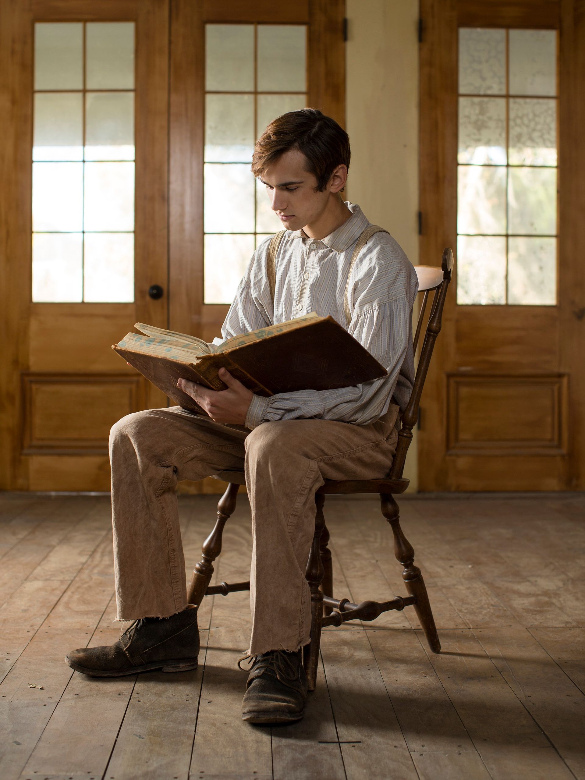 Young Joseph Smith sits in a chair reading the bible.  He is also standing holding the bible and praying about what he just read.