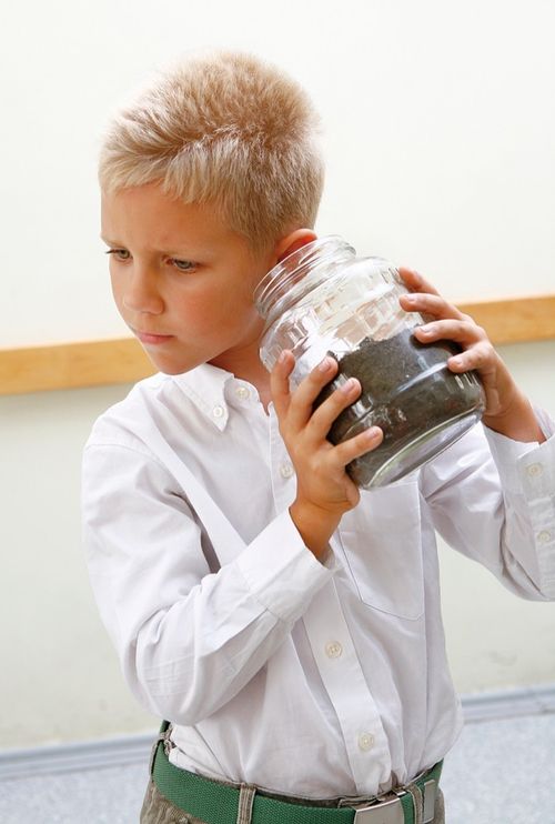 child shaking a jar filled with dirt