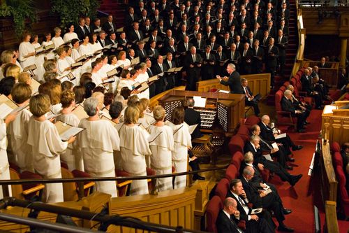 Women in white dresses and men in black suits sing in the Mormon Tabernacle Choir at the Tabernacle.