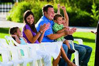 A family sitting together in the Brigham Young Historic Park.  They are sitting on white chairs set up for a concert in the park.