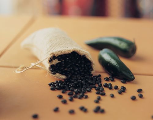 A little burlap bag full of black beans with peppers next to it.