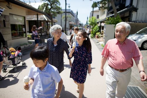An elderly couple walking outside with their grandchildren, who are eating ice cream cones.