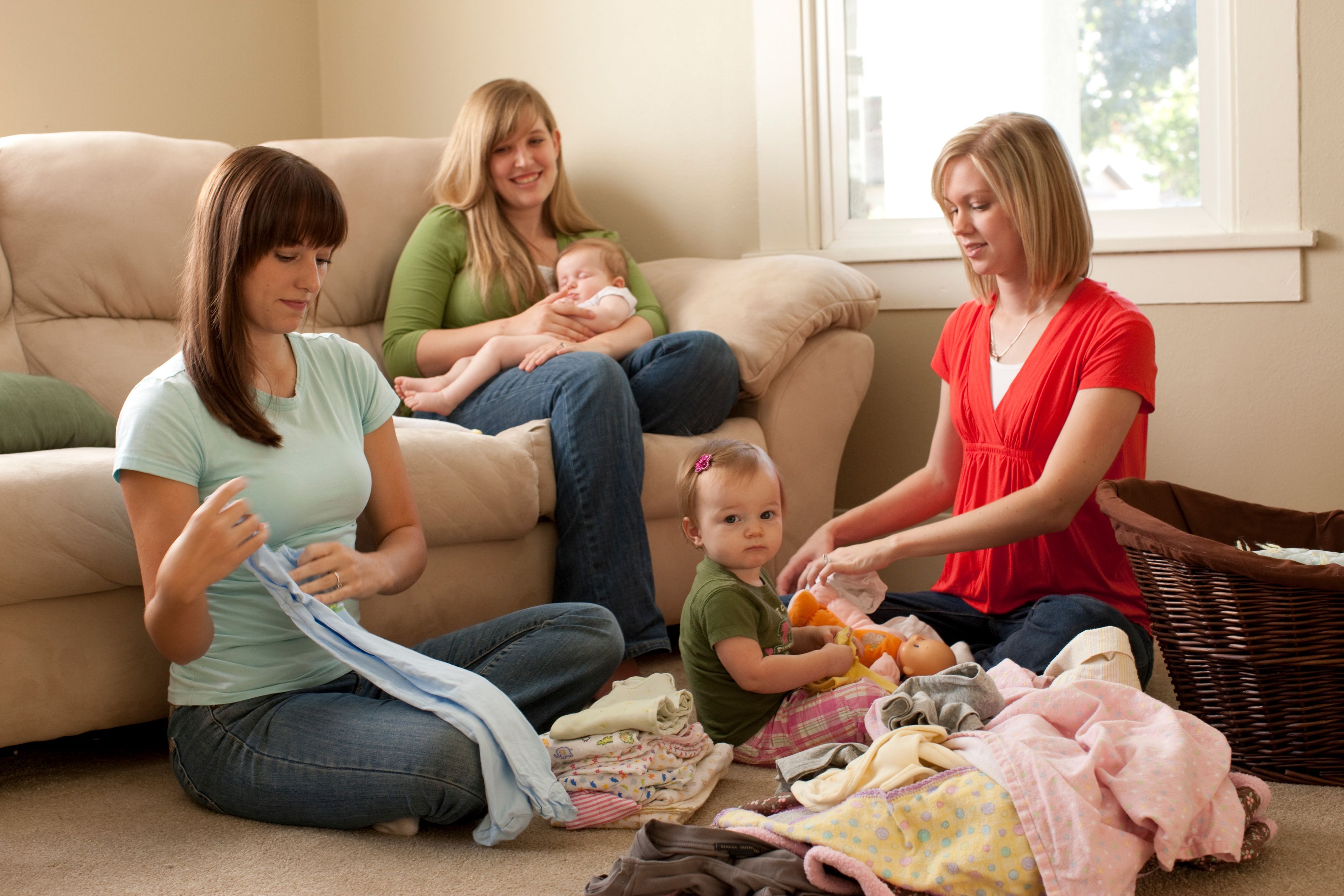 Ministering sisters help a woman with two children fold her laundry.