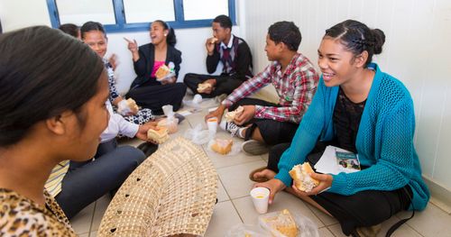 Tonga. Group of young men and young women eating.