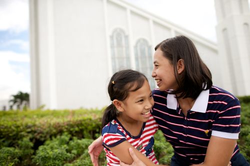A mother smiling and hugging her young daughter while sitting outside of the Manila Philippines Temple.
