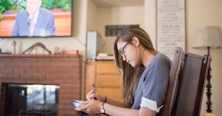 a woman takes notes while watching general conference