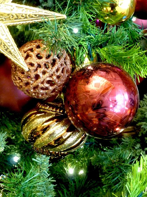 A group of red and gold ornaments on a green Christmas tree with white lights.