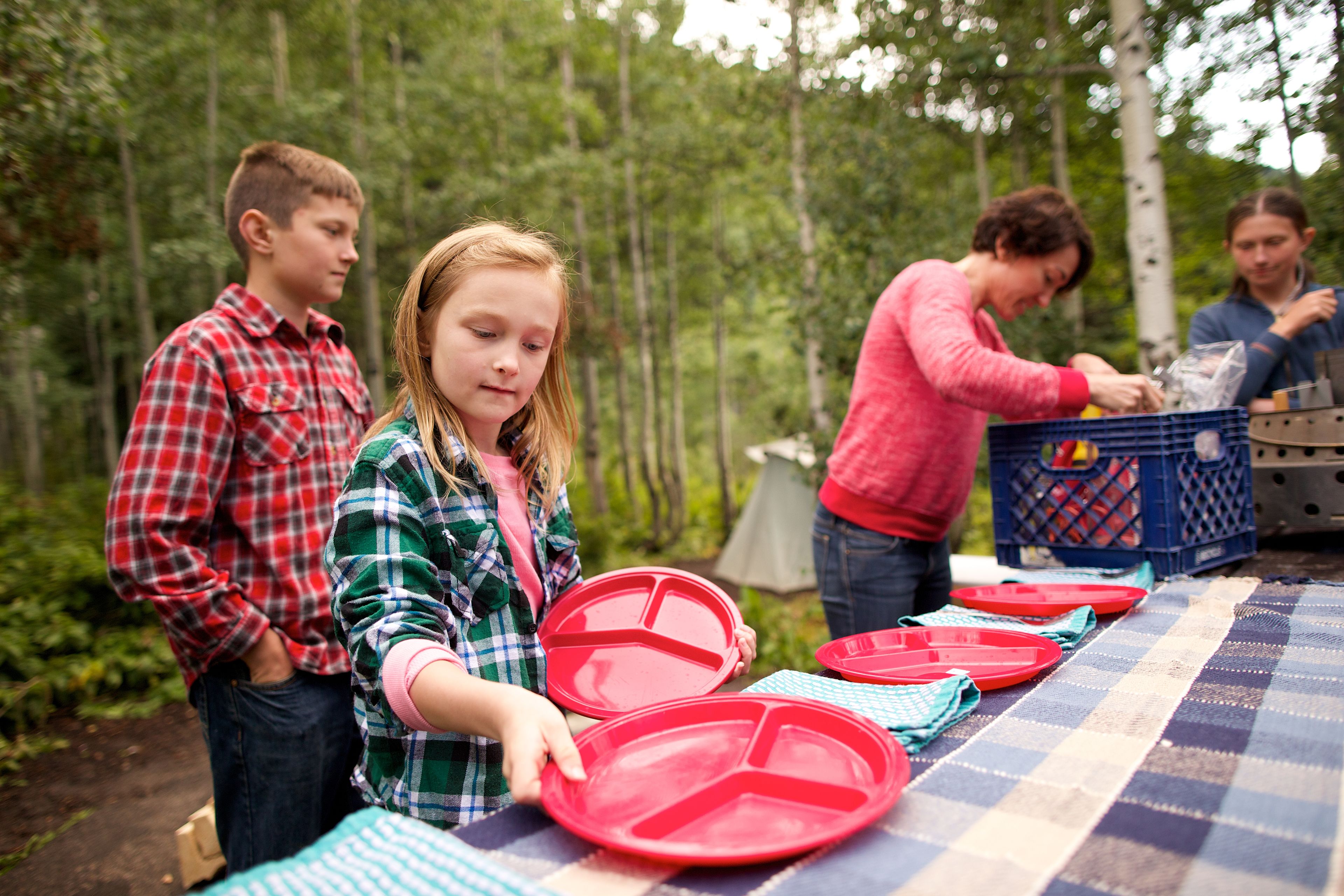 A family sets a table with plates and napkins at a campground.