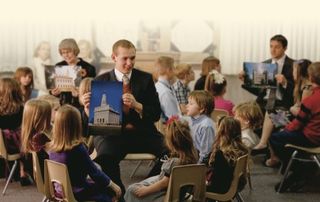 Primary teachers gathered in groups in a large room.  They are each being taught by a different teacher.