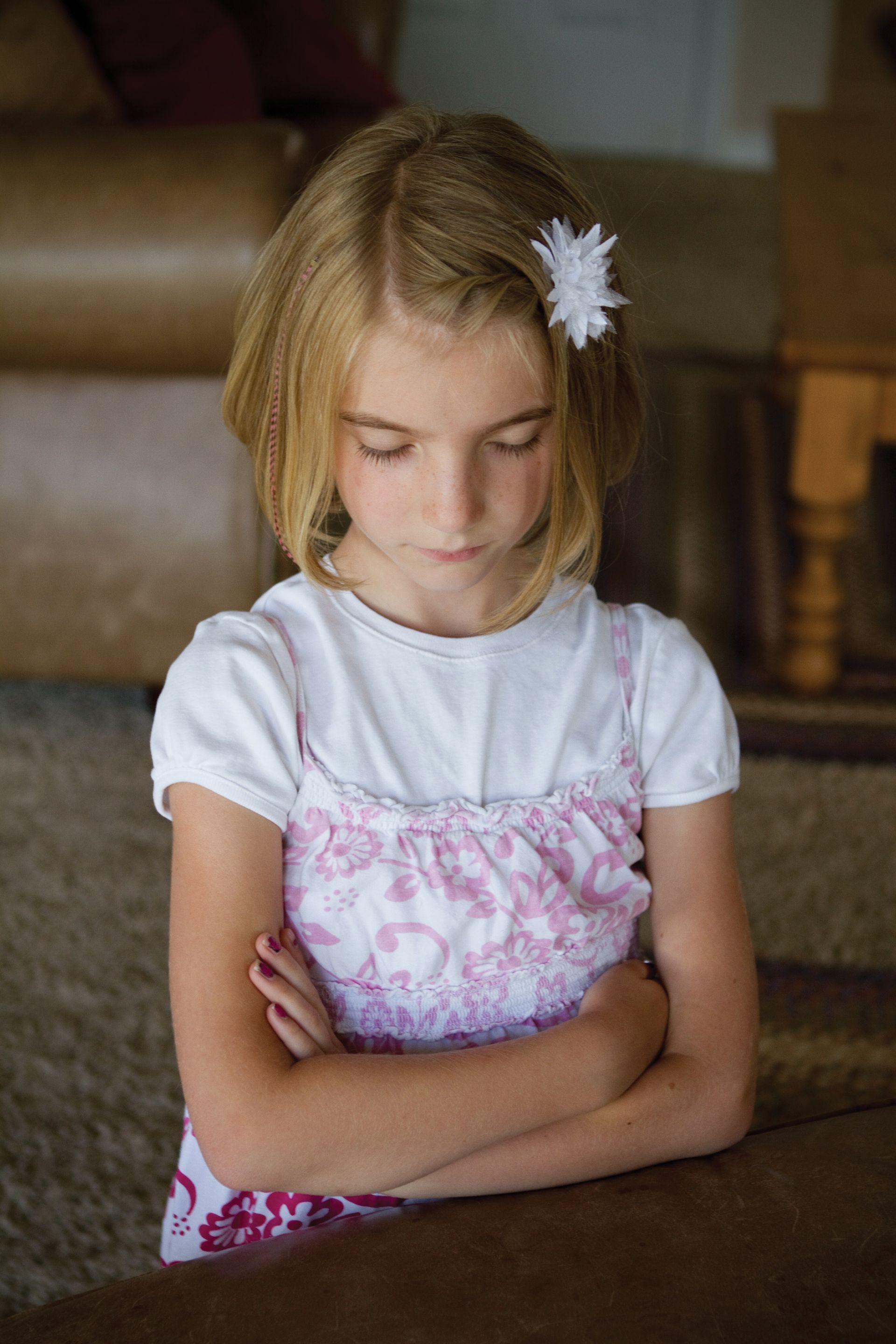 A young girl prays, kneeling in the living room.