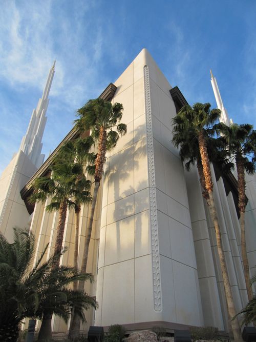The front of the Las Vegas Nevada Temple from below, with palm trees growing near the walls of the temple.