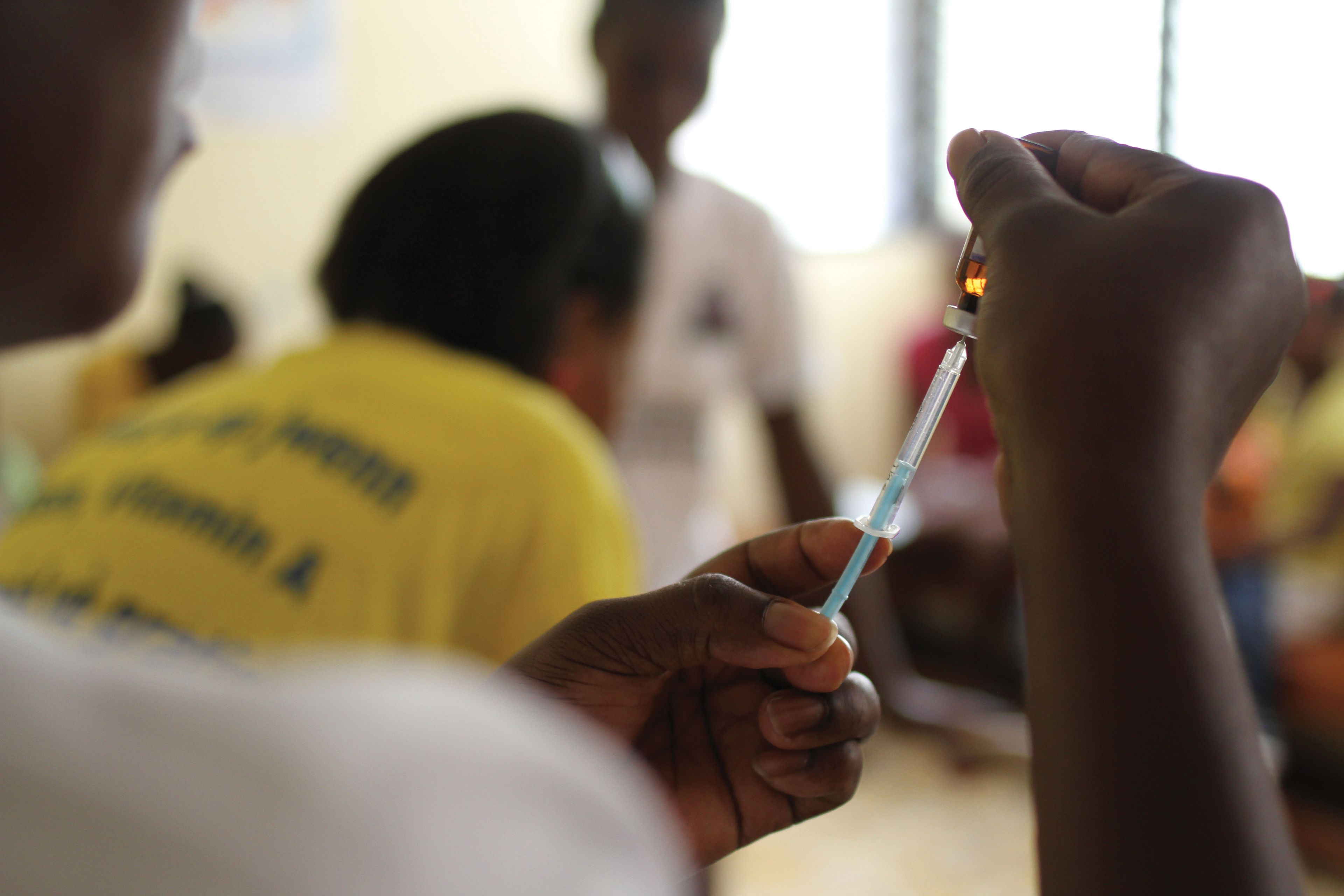 A person in Haiti holding a vaccine bottle while filling a syringe.